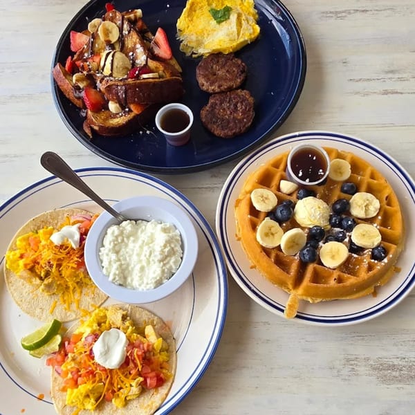 Three plates of breakfast food, including French toast, breakfast tacos, and a waffle with fruit.