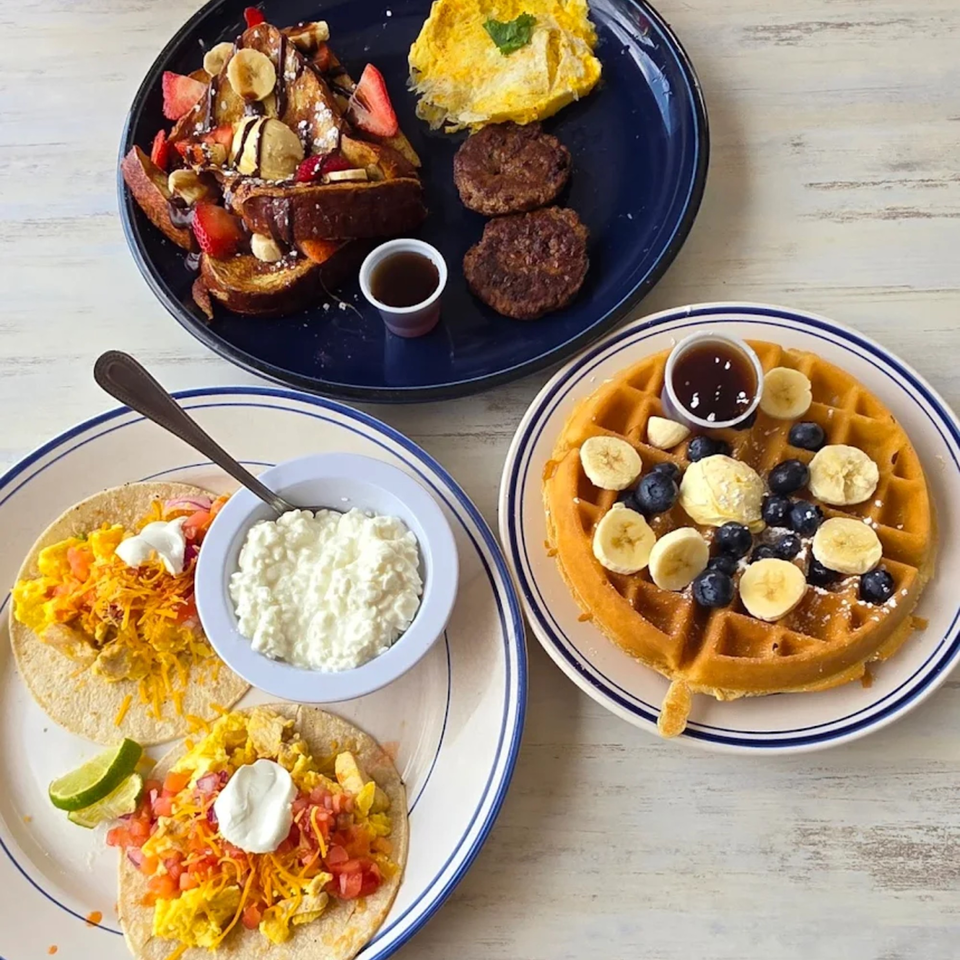 Three plates of breakfast food, including French toast, breakfast tacos, and a waffle with fruit.