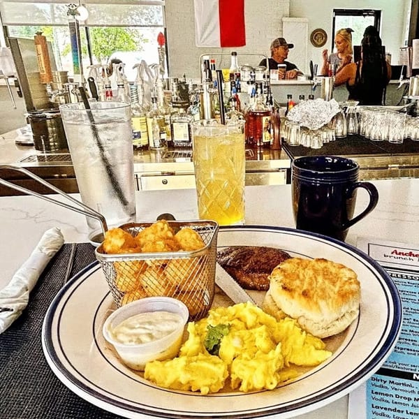 A breakfast plate with scrambled eggs, biscuit, sausage, tater tots, and dipping sauce at Anchor Allie's.