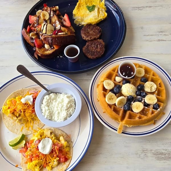 Three plates of breakfast food, including French toast, breakfast tacos, and a waffle.
