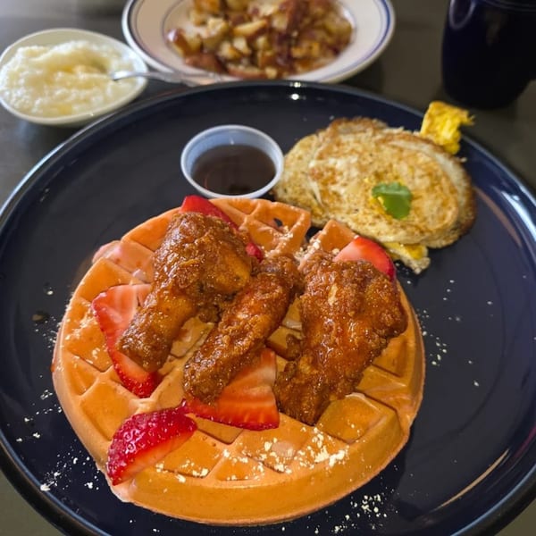 Chicken and waffles with strawberries, syrup, and a side of eggs and potatoes.